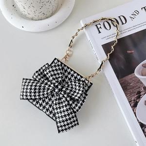 Detail of houndstooth mini bag with large bow and gold chain strap on lifestyle background