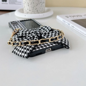 Detail of houndstooth folding phone case featuring a large bow and gold chain strap