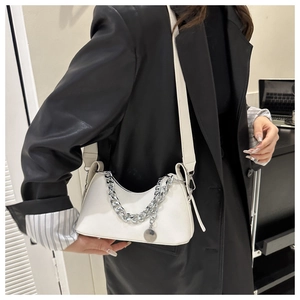 Close-up of white minimalist crescent bag with decorative silver chain on a black blazer