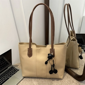 Borsa tote beige alla moda con manici marroni e ciondolo a pecora in un interno moderno