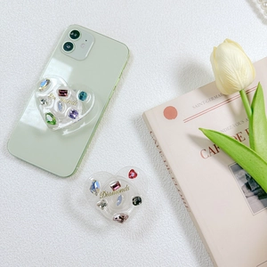Detail of a heart-shaped phone socket with colorful rhinestones on a mint green smartphone