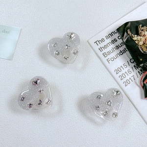 Detail von drei glitzernden Herz-Handyhalterungen mit rosa Strass auf weißem Leder