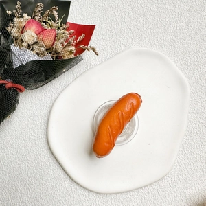 Macro detail of realistic 3D sausage phone grip on a white ceramic plate with flowers