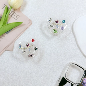 Detail of heart-shaped acrylic phone grip with colorful rhinestones and gold text