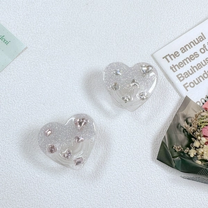 Detail von herzförmigen Glitzer-Handyhalterungen mit rosa Strasssteinen auf weißer Fläche