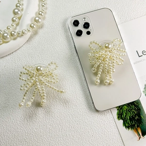Elegant pearl bow-shaped expandable phone grip holder attached to a white smartphone