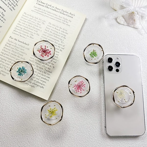 Close-up of dried flower resin phone grips with gold edges on a white smartphone