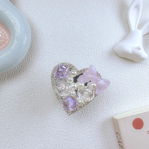 Detailed view of a purple crystal heart phone grip with pearls and a ribbon bow charm