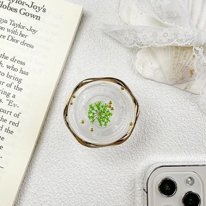 Detail of round phone grip featuring gold wavy edges and green dried flowers in resin