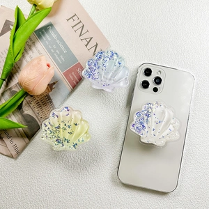 Glitter seashell phone grip sockets in iridescent white, blue, and yellow on white table