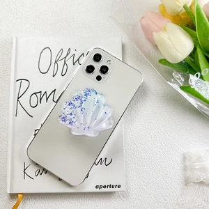 White shell-shaped phone grip with glitter and purple accents on a silver smartphone