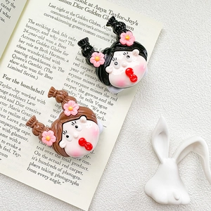 Detail of two cartoon girl resin accessories with pink flowers on an open book background