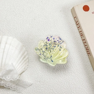 Macro detail of shell-shaped phone grip with pearls and glitter on a white texture