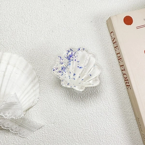 Detail of seashell-shaped phone grip with blue glitter sequins on a textured surface