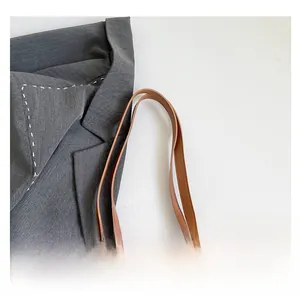 Detail view of brown tote bag handles with white graffiti pattern on smooth leather