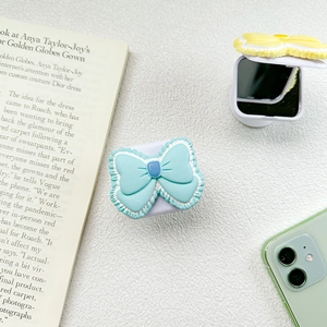Close-up of bow-shaped phone grip with flip-up vanity mirror in pastel blue and yellow