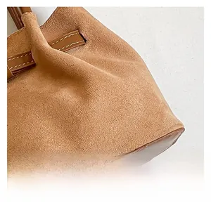 Close-up of brown suede bucket bag with smooth leather trim and white contrast stitching