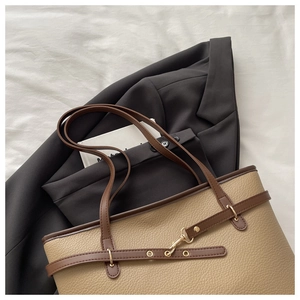Detail of beige lychee leather tote bag with brown straps over a grey blazer jacket