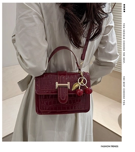 Detail of burgundy crocodile-textured handbag featuring a cute cherry charm and metal clasp