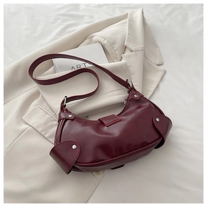 Detail of burgundy half-moon underarm bag with silver rivets on beige blazer