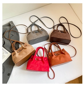 Flat lay of multiple suede bucket bags in gray, brown, and red with metallic buckles