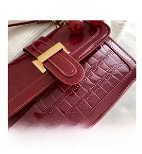 Close-up of burgundy crocodile pattern leather handbag with iconic golden H-shaped clasp