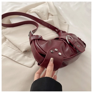 Detail of burgundy PU leather hobo bag with silver buckles and adjustable strap on white fabric