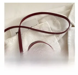 Detail of adjustable strap and cherry pendant on burgundy faux crocodile bag
