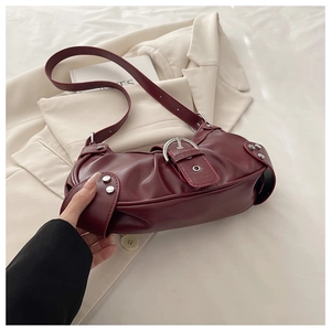 Detail of burgundy faux leather bag with silver buckle and matte texture on cream blazer