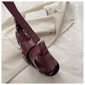 Detail of dark red PU bucket bag featuring silver buckles and rivets on white fabric