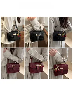 Detail of crocodile embossed crossbody bag with gold H-buckle and cherry charm