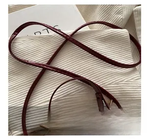 Detail of adjustable wine red patent leather shoulder strap with gold metal buckles