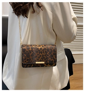 Detail of leopard print baguette bag with gold chain strap on a white blazer