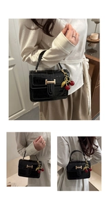 Detail of black crocodile embossed handbag with gold H-buckle and cherry charm accessory