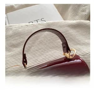 Detail of burgundy patent leather handbag featuring gold metal twist lock and handle