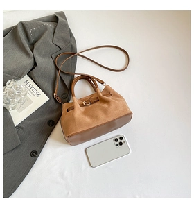 Sac seau en daim marron avec lanières en cuir et boucle métal près d'un smartphone