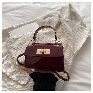 Detail der weinroten Lackleder-Handtasche mit goldenem Drehverschluss und Griff