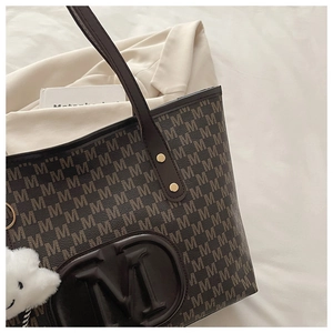 Detail of printed tote bag with M letter pattern, leather pocket and cloud pendant