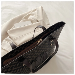 Detail view of large brown tote bag with M-pattern print and leather shoulder straps