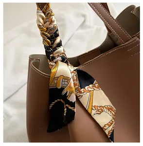 Gros plan d'un foulard en soie à motif chaîne enroulé autour d'une anse en cuir