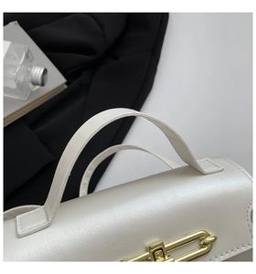 Detail of white leather handbag featuring elegant gold metal buckle and handle