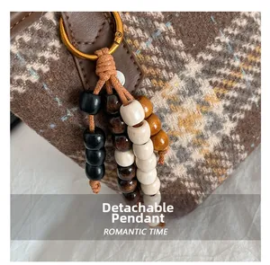 Dettaglio di ciondolo in perle di legno multicolore con anello dorato su borsa a quadri