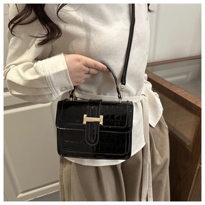 Detail of black crocodile pattern patent leather bag with gold buckle on model