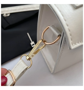 Close-up of golden hardware and textured leather stitching on a white shoulder bag
