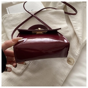 Nahaufnahme der burgunderroten Lackledertasche mit goldener Schnalle auf weißem Blazer
