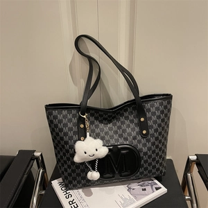 Detail of printed tote bag with M logo, slim black straps and a plush cloud charm