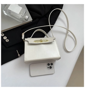 White minimalist leather satchel with golden clasp shown next to a smartphone for scale