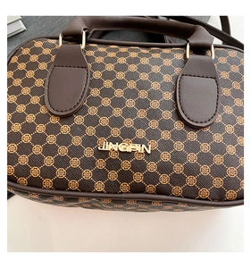 Close-up of brown Boston bag showing clover pattern and golden brand lettering detail
