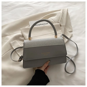 Detail of grey square handbag with woven texture flap and golden metal hardware
