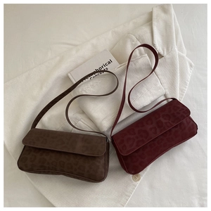 Detailed view of dark brown and burgundy leopard print baguette bags on textured fabric